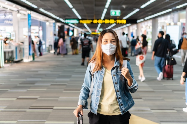 Jonge aziatische vrouw die met gezichtsmasker bij luchthaventerminal loopt. gezondheidszorg en bescherming concept.