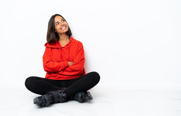 Jonge Aziatische vrouw die met rolschaatsen op de vloer omhoog kijkt terwijl het glimlachen