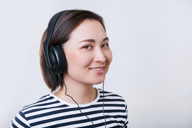 Jonge aziatische vrouw die muziek luistert met zwarte hoofdtelefoon