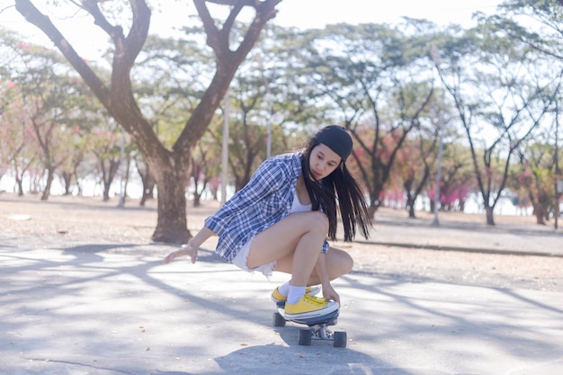 Jonge Aziatische vrouw die old-school skateboard berijdt bij skatepark