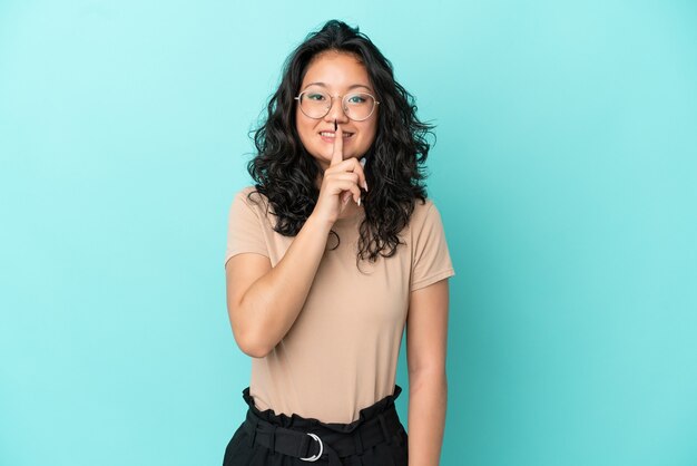 Jonge aziatische vrouw die op blauwe achtergrond wordt geïsoleerd die een teken van stiltegebaar toont dat vinger in mond zet