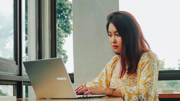 Jonge Aziatische vrouw die op een laptop werkt terwijl ze in het café zit en door documenten kijkt