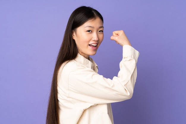 Jonge Aziatische vrouw die op purpere muur sterk gebaar doet
