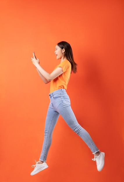 Jonge Aziatische vrouw die oranje T-shirt draagt die op sinaasappel springt