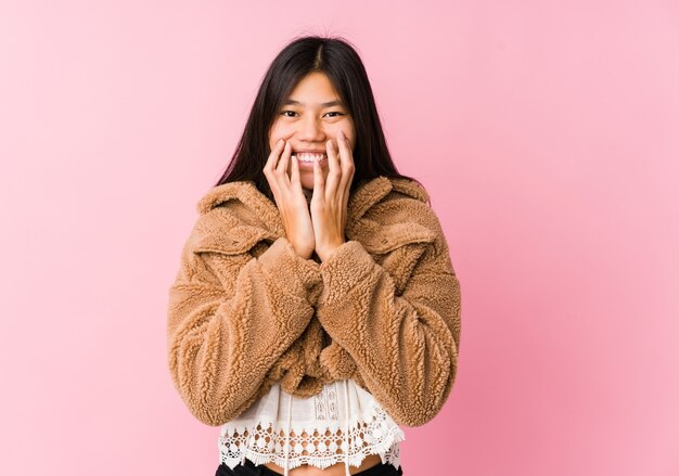 Jonge Aziatische vrouw die over iets lacht, mond behandelt met handen.