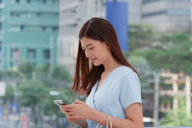 Jonge Aziatische vrouw die smartphone gebruiken tijdens het lopen bij buitenkant.