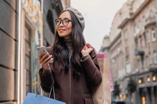 Jonge aziatische vrouw die smartphone gebruikt en naar de showcase kijkt terwijl ze geniet van een dagje winkelen