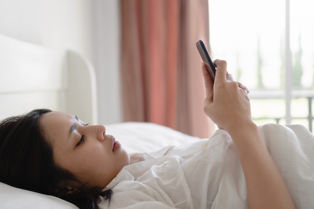 Jonge Aziatische vrouw die smartphone met het lege scherm gebruiken terwijl het liggen in bed bij ochtend.