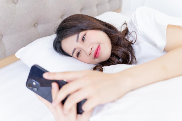 Jonge aziatische vrouw die smartphone op bed gebruikt