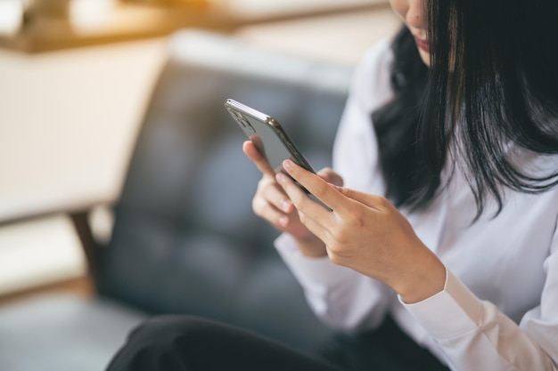 Jonge aziatische vrouw die SMS-bericht typt op een smartphone in een café