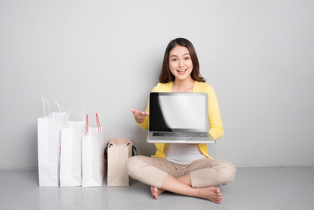 Jonge aziatische vrouw die thuis online winkelt naast een rij boodschappentassen