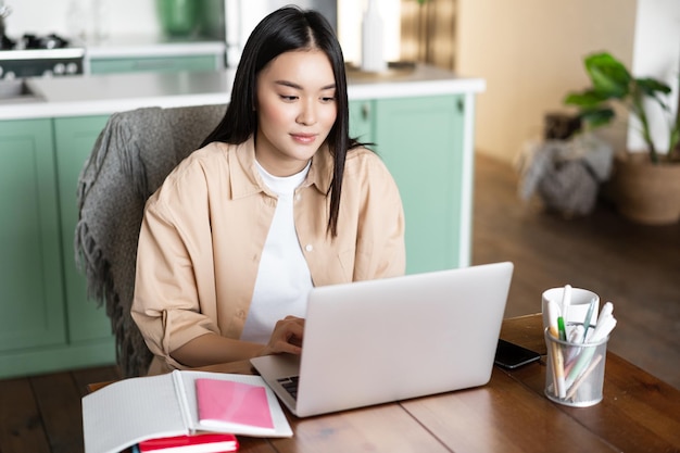 Jonge aziatische vrouw die thuis zit met laptop die online videochat bestudeert tijdens schoolklassen d...