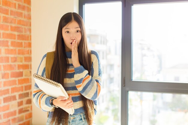 Jonge Aziatische vrouw die zich ongerust, boos en bang voelt, de mond bedekt met handen, er angstig uitziet en het verknoeid heeft