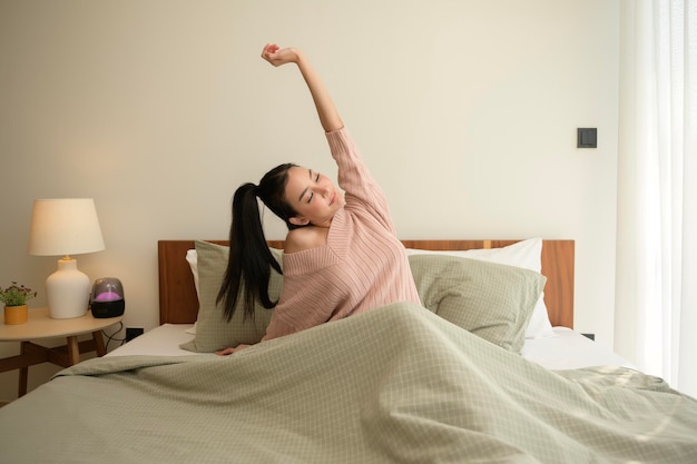Jonge Aziatische vrouw die zich uitstrekt in bed na het opstaan in de ochtend