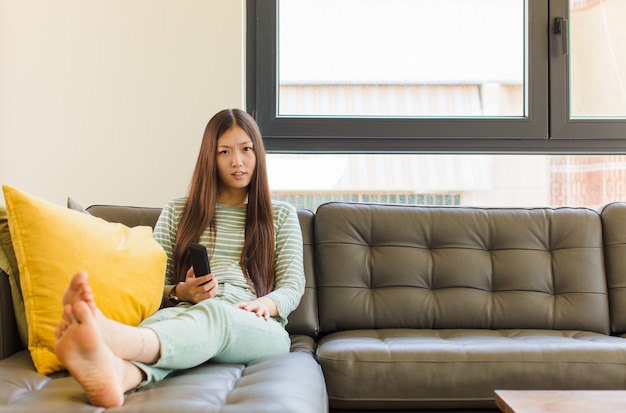 Jonge aziatische vrouw die zich verbaasd en verward voelt, met een domme, verbijsterde uitdrukking op zoek naar iets onverwachts