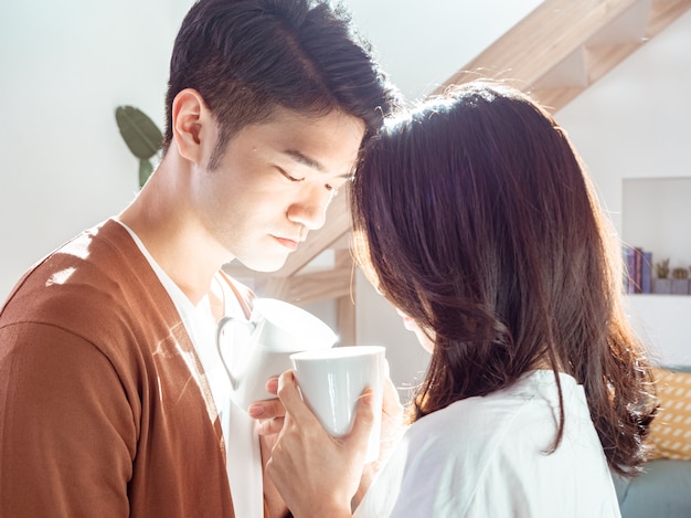 Jonge aziatische vrouw en man genieten van tijd samen thuis doorbrengen met een kopje koffie in handen.