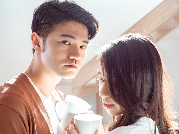 Jonge aziatische vrouw en man genieten van tijd samen thuis doorbrengen met een kopje koffie in handen.