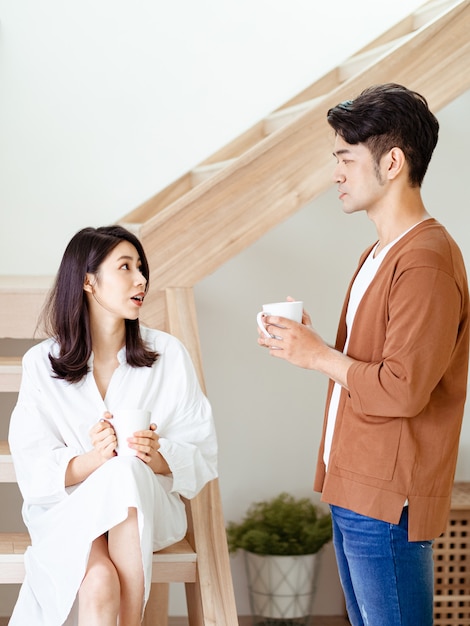 Jonge aziatische vrouw en man genieten van tijd samen thuis doorbrengen met een kopje koffie in handen.