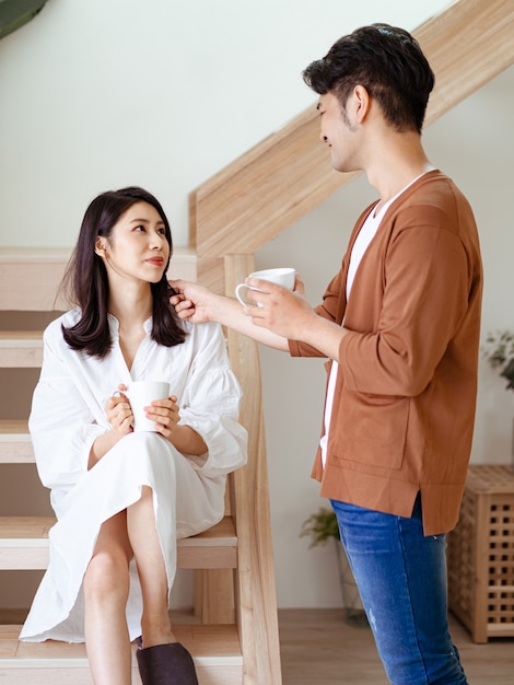 Jonge aziatische vrouw en man genieten van tijd samen thuis doorbrengen met een kopje koffie in handen.