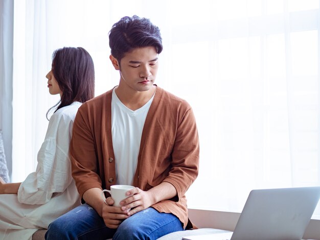 Jonge Aziatische vrouw en man thuis met kopje koffie in handen.