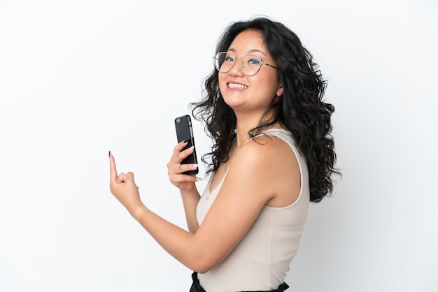 Jonge Aziatische vrouw geïsoleerd op een witte achtergrond met behulp van mobiele telefoon en terug te wijzen