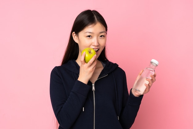 Jonge Aziatische vrouw geïsoleerd op roze achtergrond met een fles water en het eten van een appel