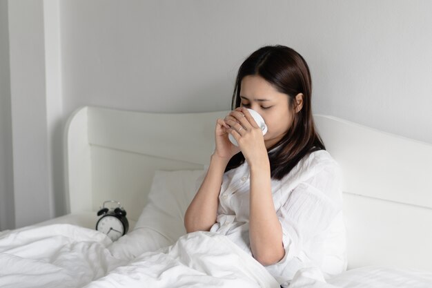 Jonge Aziatische vrouw het drinken ochtendkoffie in bed.