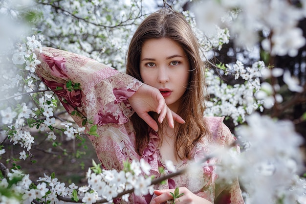 Jonge Aziatische vrouw in een bloeiende tuin. romantisch beeld van stijlvolle casual vrouw, trendy zijden blouse. positieve stemming. Vrolijke Bloesem volle bloei in Japan.