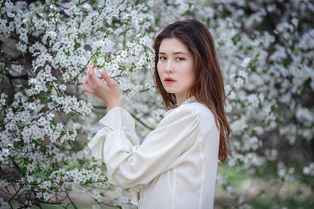 Jonge Aziatische vrouw in een bloeiende tuin. romantisch beeld van stijlvolle casual vrouw, trendy zijden blouse. positieve stemming. Vrolijke Bloesem volle bloei in Japan.