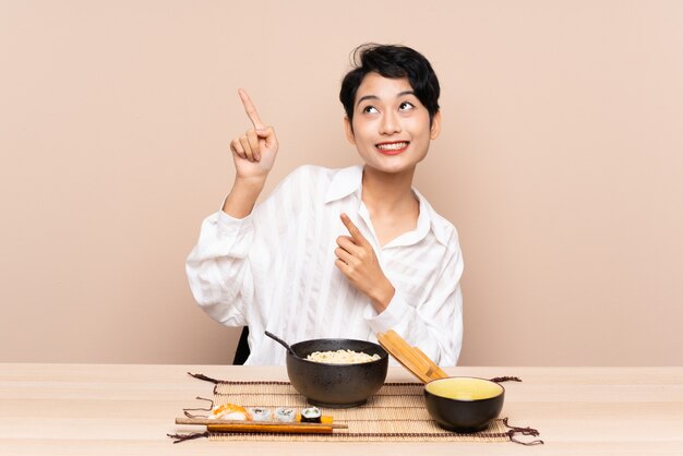 Jonge Aziatische vrouw in een lijst met kom van noedels en sushi die met de wijsvinger een geweldig idee richten