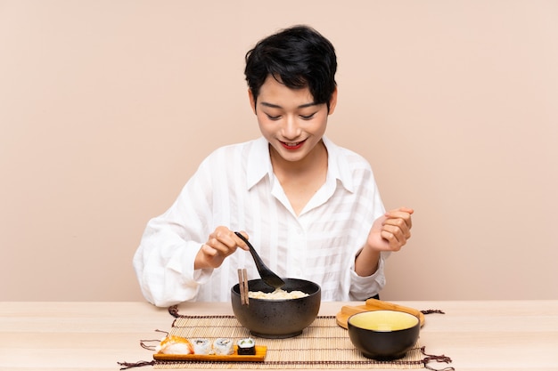 Jonge Aziatische vrouw in een tafel met kom noedels en sushi