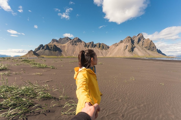 Jonge Aziatische vrouw in gele jas hand in hand met vriendje op het strand met Vestrahorn berg in Viking dorp op Stokknes in IJsland