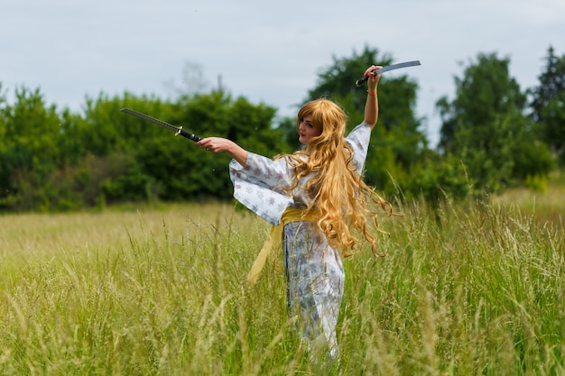 Jonge aziatische vrouw in traditionele kimono traint vechttechnieken met katana-zwaard buitenshuis, samoerai-krijgermeisje