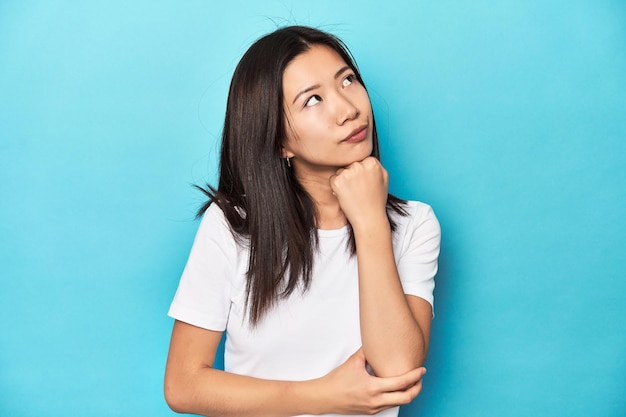Jonge Aziatische vrouw in witte t-shirt studio opname denken en opzoeken reflecterend