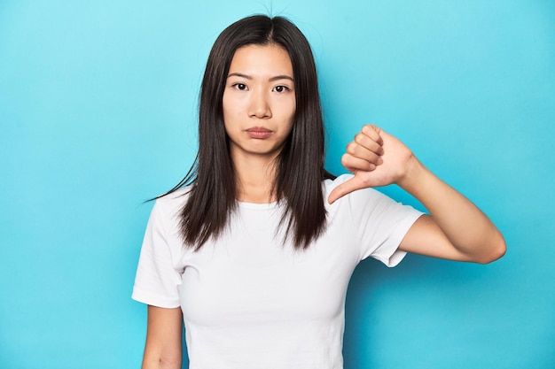 Jonge Aziatische vrouw in witte t-shirt studio opname met een afkeer gebaar duimen naar beneden