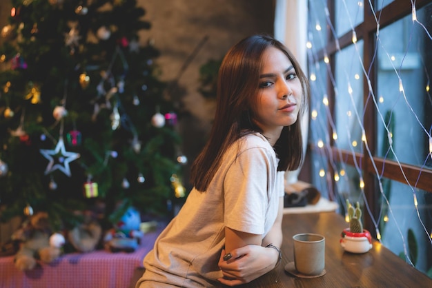 Jonge Aziatische vrouw is blij en geniet ervan om kerstavond te vieren in café Kerstfeest lichte achtergrond in koffiecafé