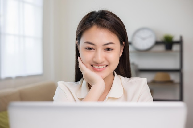 Jonge Aziatische vrouw met behulp van laptop chatten videoconferentie online zittend in de woonkamer thuis Zakenvrouw kijken naar scherm Vergadering op sociale media live stoom Werk leren vanuit huis