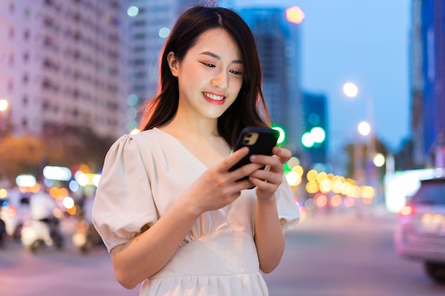 Jonge Aziatische vrouw met behulp van smartphone op straat 's nachts