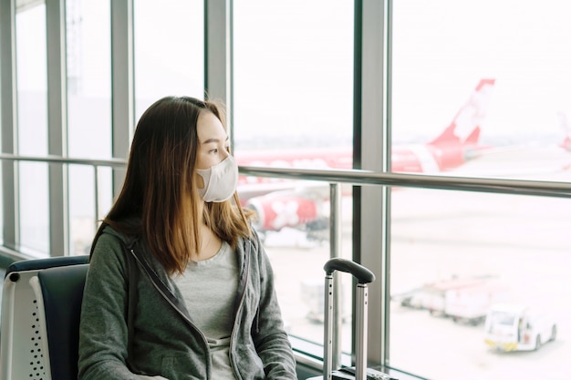 Jonge Aziatische vrouw met chirurgische masker gezicht bescherming zittend op de luchthaventerminal. Bescherming Coronavirus / Covid-19 en luchtverontreiniging pm2.5 concept.