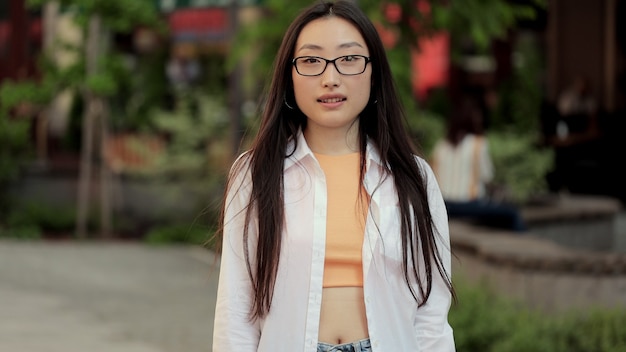 Jonge aziatische vrouw met een bril die naar de camera glimlacht en naar de straat kijkt, aantrekkelijke gelukkige aziatische vrouw kruist haar armen close-up portret