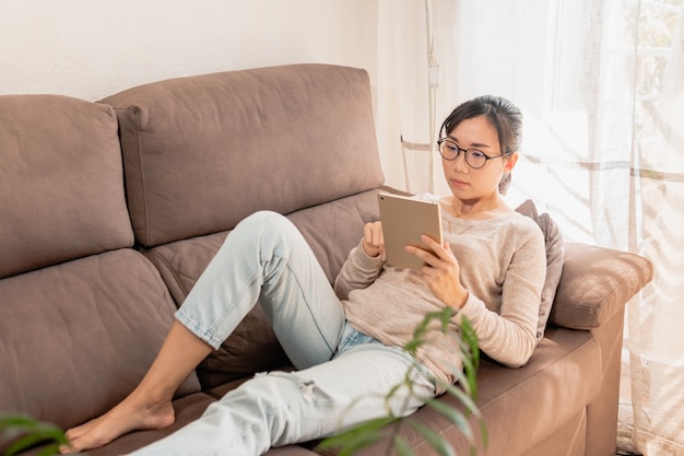 Jonge Aziatische vrouw met een bril met behulp van een tablet op de bank.