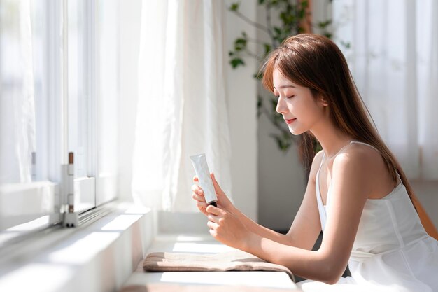 Jonge Aziatische vrouw met een cosmetische tube in haar hand Productmodel