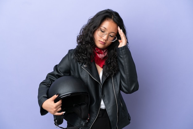 Jonge Aziatische vrouw met een motorhelm geïsoleerd op paarse achtergrond met hoofdpijn