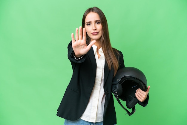 Jonge Aziatische vrouw met een motorhelm over geïsoleerde chroma key achtergrond die stopgebaar maakt