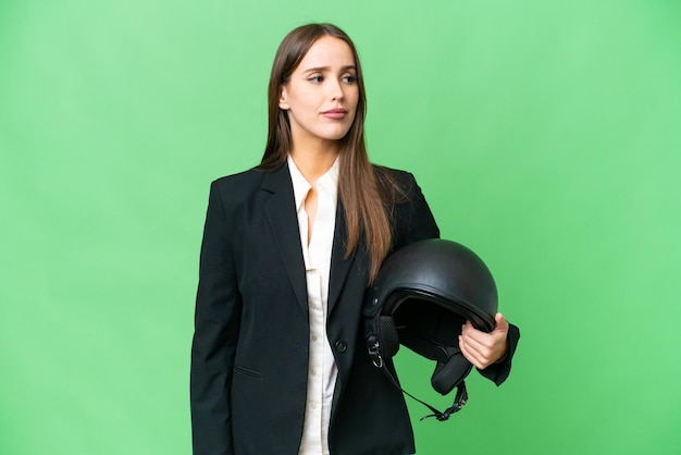 Jonge Aziatische vrouw met een motorhelm over geïsoleerde chroma key achtergrond kijkend naar de zijkant