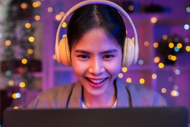 Foto jonge aziatische vrouw met een vrolijke glimlach luistert naar muziek van gele koptelefoons en handen met laptop op vakantie in huis