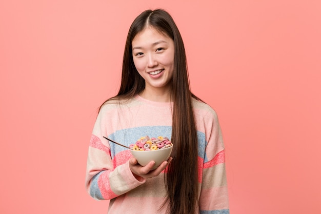 Jonge Aziatische vrouw met graangewassenkom glimlachen zeker met gekruiste wapens.