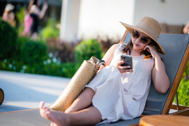 Jonge Aziatische vrouw met hoed ontspannen naast het zwembad bij luxe hotelreizen en zomerconcept