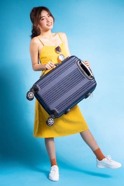 Jonge Aziatische vrouw met koffer op blauw, zomer concept