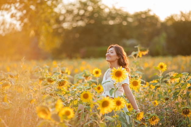 Jonge Aziatische vrouw met krullend haar in een veld met zonnebloemen bij zonsondergang.